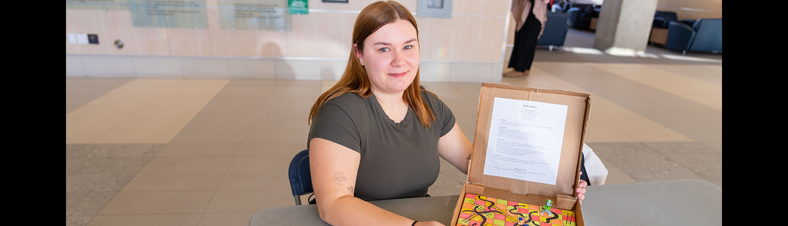 Erin Jackman sits at a table holding a colourful prototype of the game she created