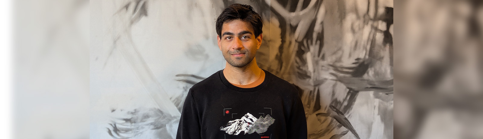 Taij Mann wears a black shirt and stands in front of a wall with black and white marbling.