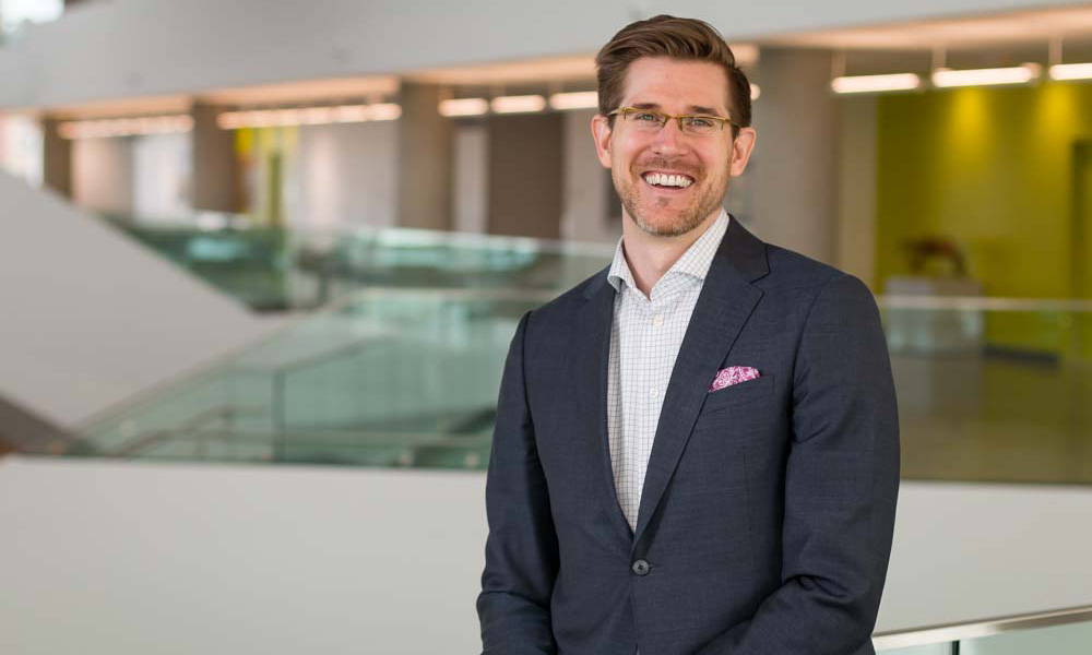 Dr. Robert Andruchow stands near the glass railing on the second floor of Allard Hall, smiling.