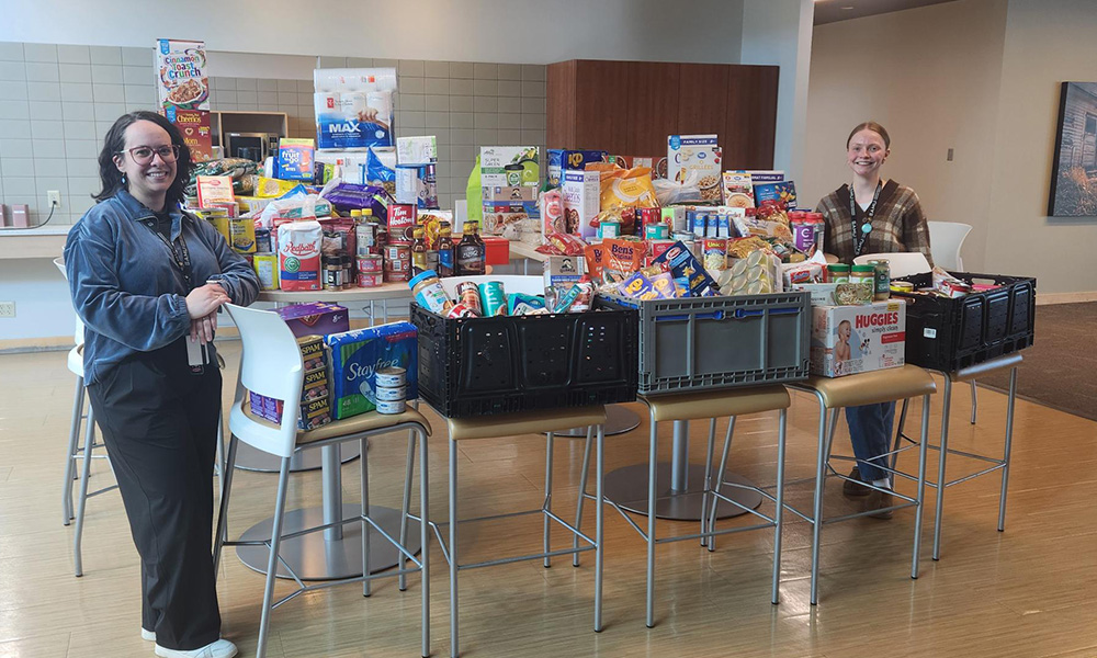 Two individuals from SAMU stand with a table loaded with donations to the student food bank
