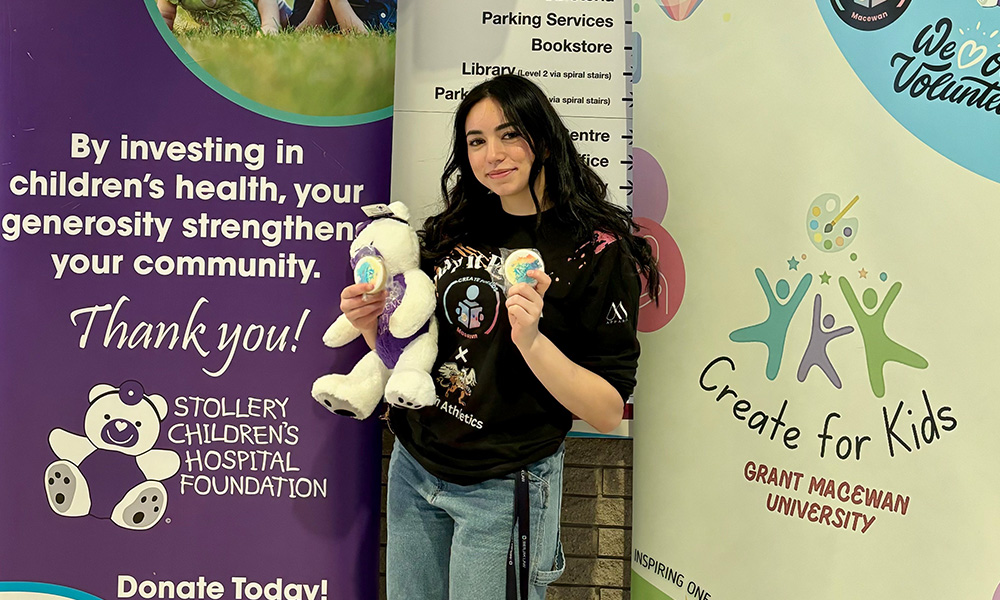Amanni Chaaban holds a teddy bear and cookies while standing in front of a Stollery Children's Hospital Foundation display