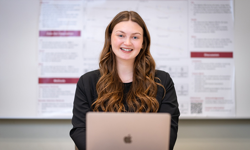 Brynn O'Connell sits behind a laptop and in front of her research poster