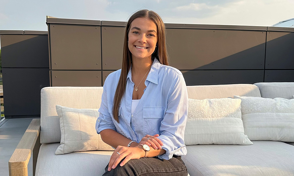Lauren Tkalcic sits outdoors on a white sofa wearing a blue shirt