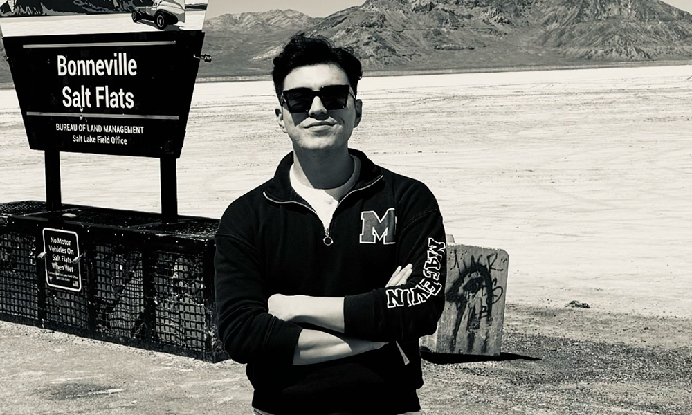 Brian Young wears sunglasses and stands in front of a sign that says Bonneville Salt Flats