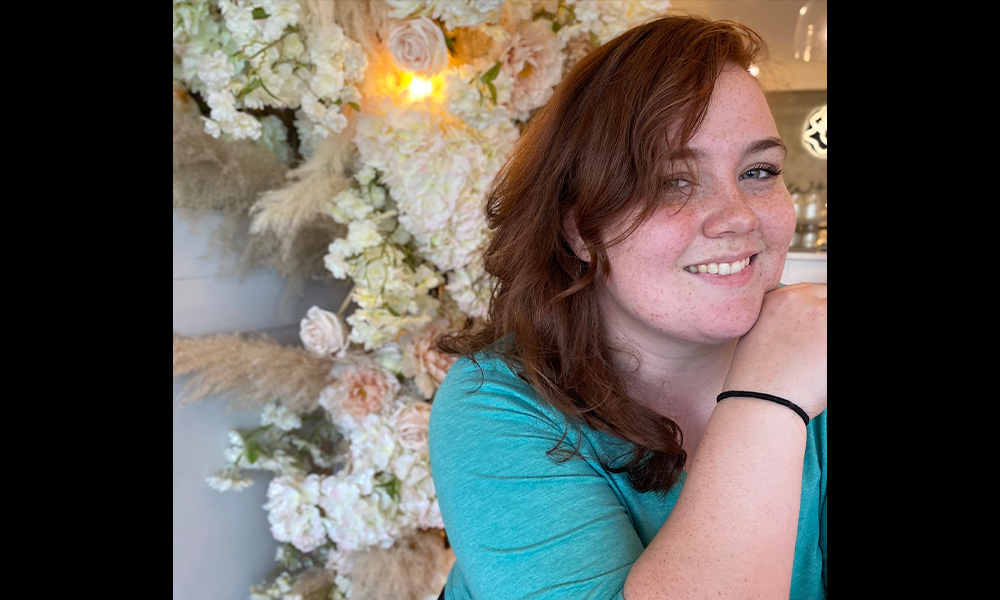 A woman sits in front of a large floral arrangement, smiling.
