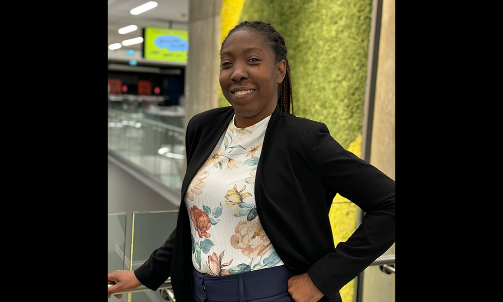 A woman in a black blazer stands in front of the moss wall in the SAMU Building on campus.