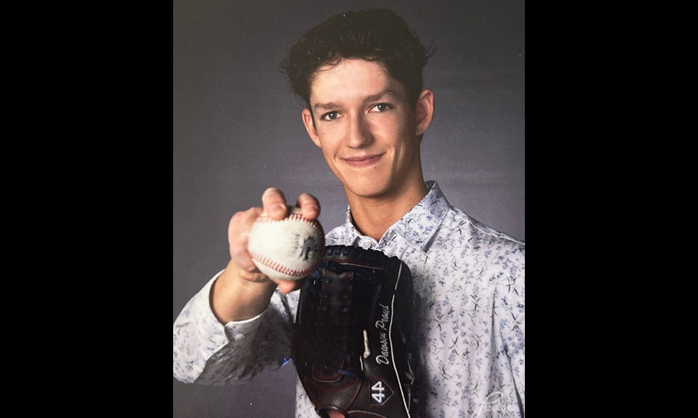 A man holds a baseball up for the camera while showing a monogrammed baseball glove on this other hand.