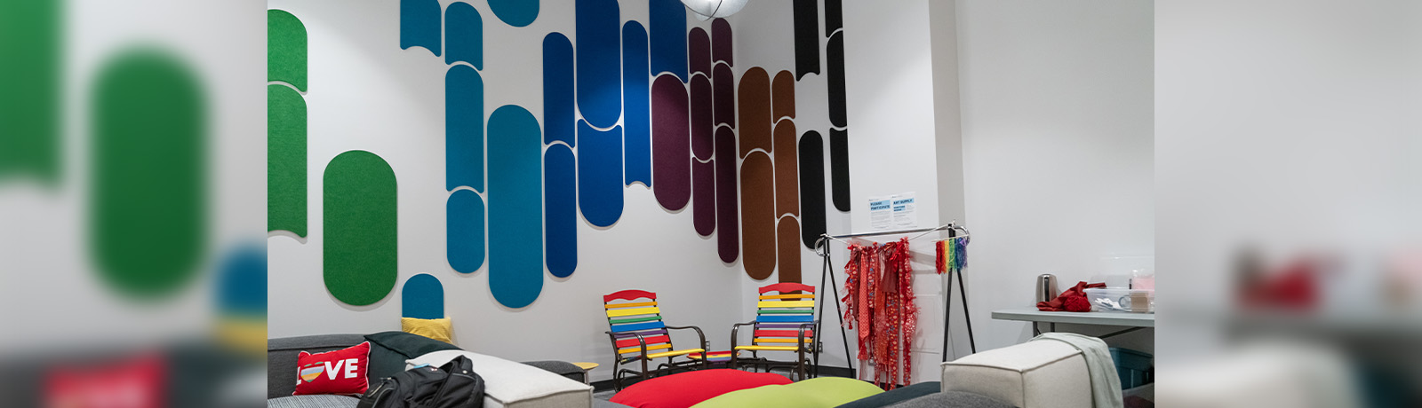 A look inside the CSGD space, with bright colours on the walls, rainbow-painted lawn chairs and cushions on a grey couch that read "love".