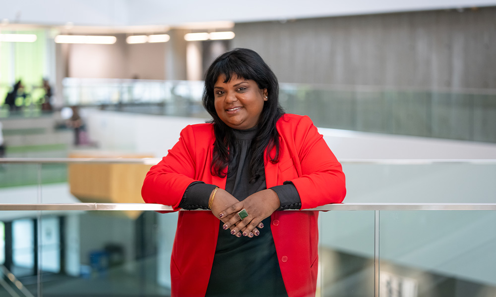 Soni Dasmohapatra leans forward against a glass railing, wearing a bright red cardigan.