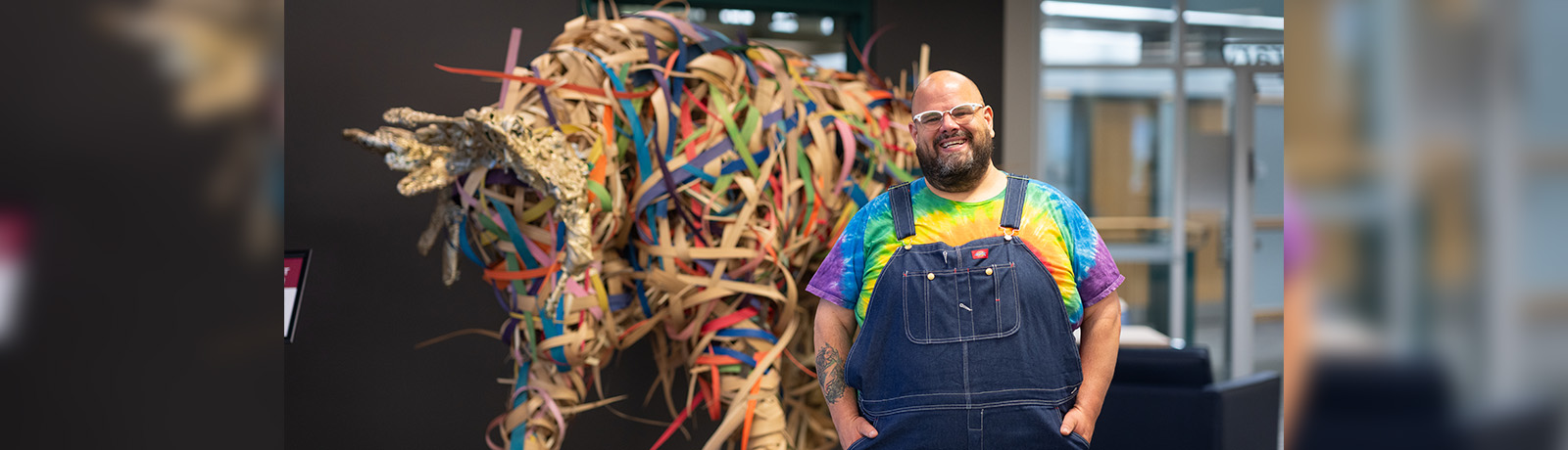 Clinton Minault stands in front of a colourful  moose sculpture in the library.