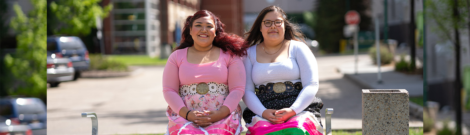 Shazeda Stamp and Emma Rain sit on a bench outside of the kihew waciston Indigenous Centre