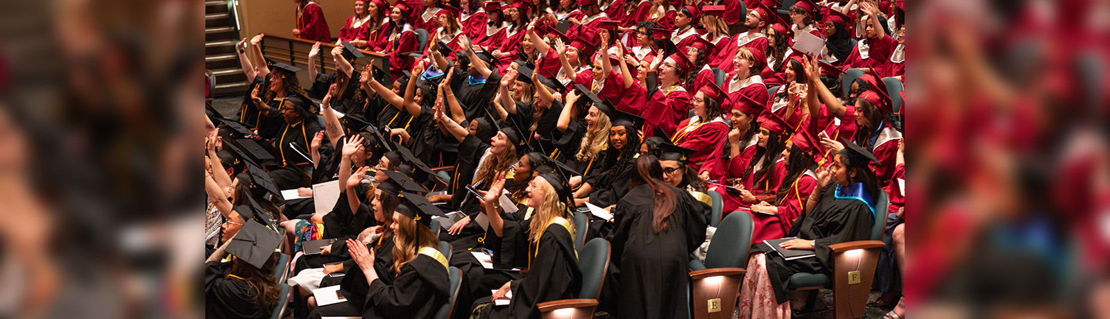 People in caps and gowns smile and wave toward the stage in the Winspear Centre.