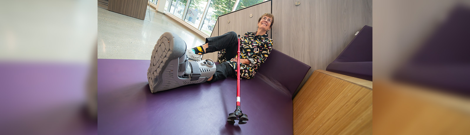 Dr. Trimbee sits on a bench on the SAMU Building stairs, holding a cane and wearing a compression boot on one leg.