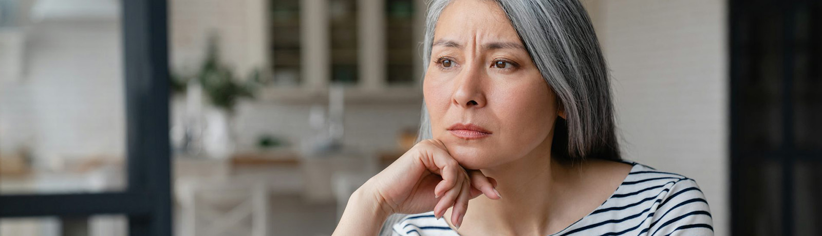 A woman with grey hair rests her chin in her hand