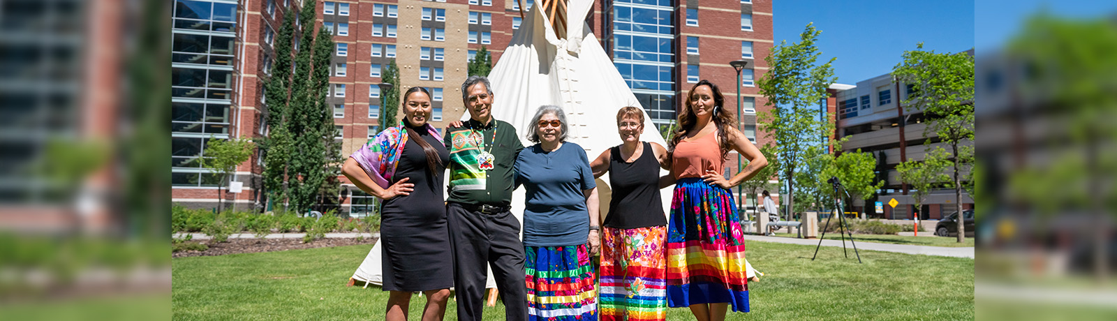 A group of people with their arms around their shoulders standing in front of a tipi