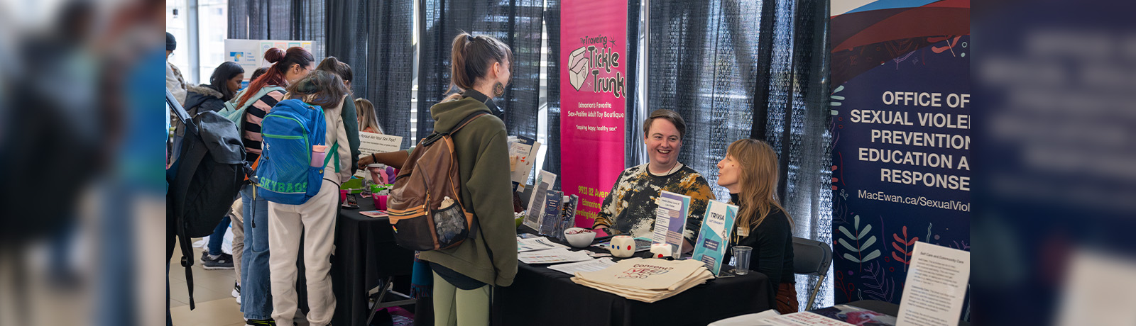 A student speaks with two people sitting at an info booth table.