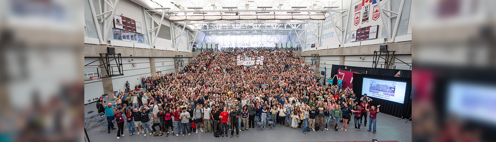 A gymnasium full of students all standing up with arms above their heads