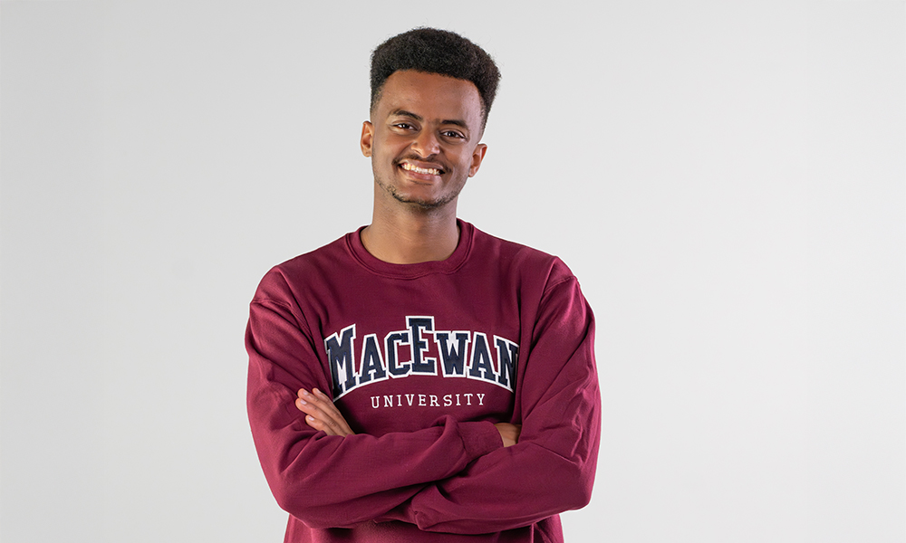 a man who is smiling at the camera stands with his arms crossed.