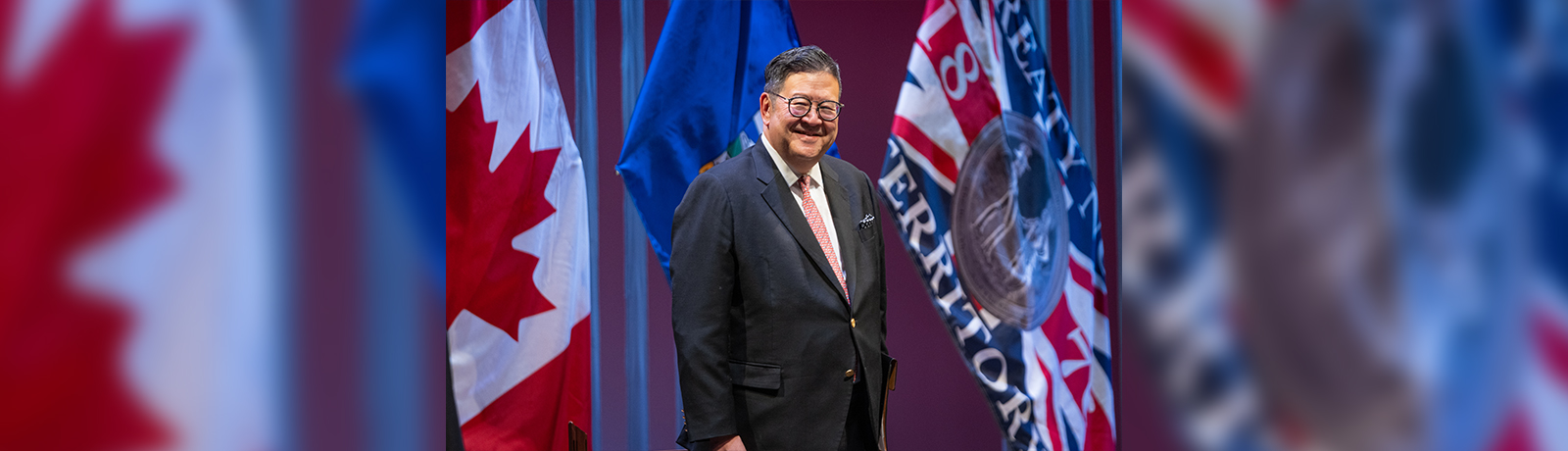A man stands on a stage flanked by flags