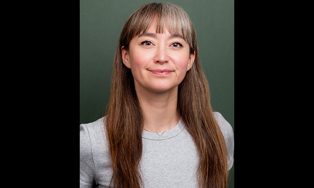 A woman with two-toned bangs wears a grey shirt and smiles.