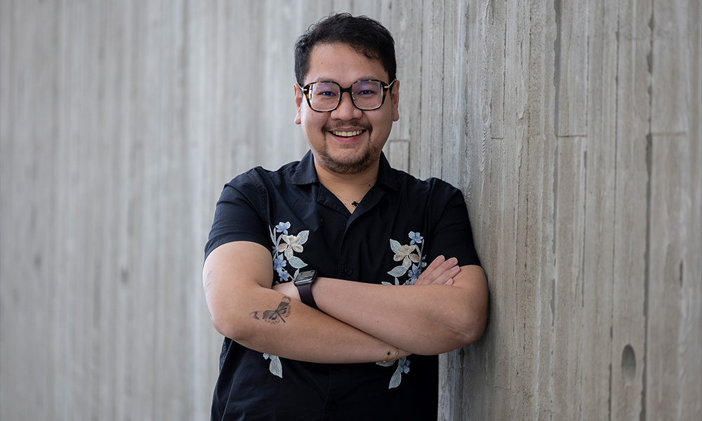 A man leans against a concrete wall, arms folded over his chest, smiling.