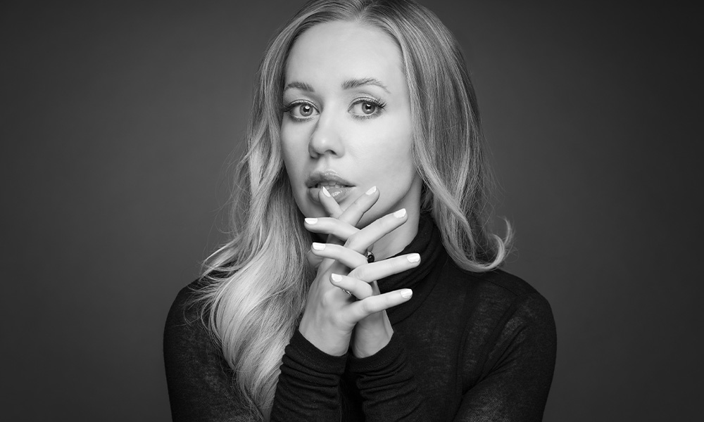 A black-and-white photo of a woman in a black shirt, hands folded in front of her.