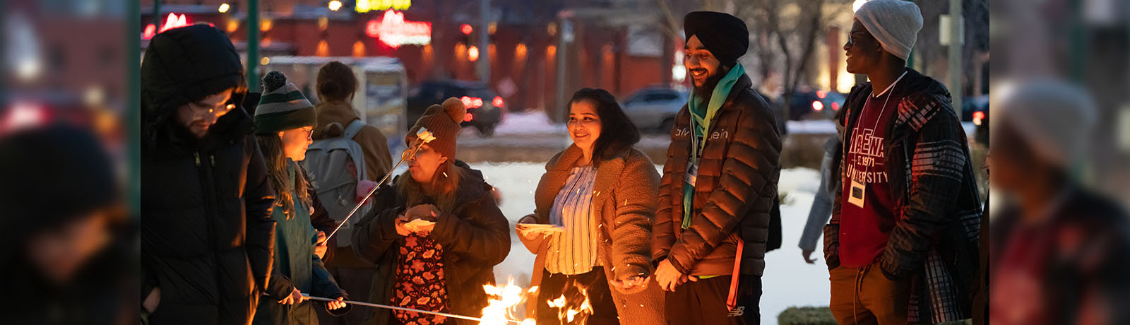 A group of students roast marshmallows over a fire pit