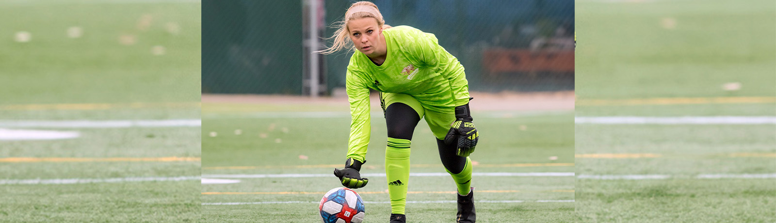 mily Burns leans down toward a soccer ball, wearing a fluorescent green soccer uniform