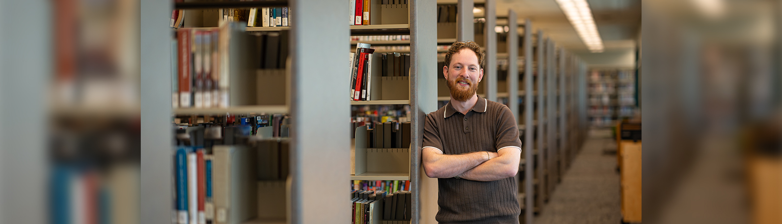 A man leaning against one row of bookshelves in a library.
