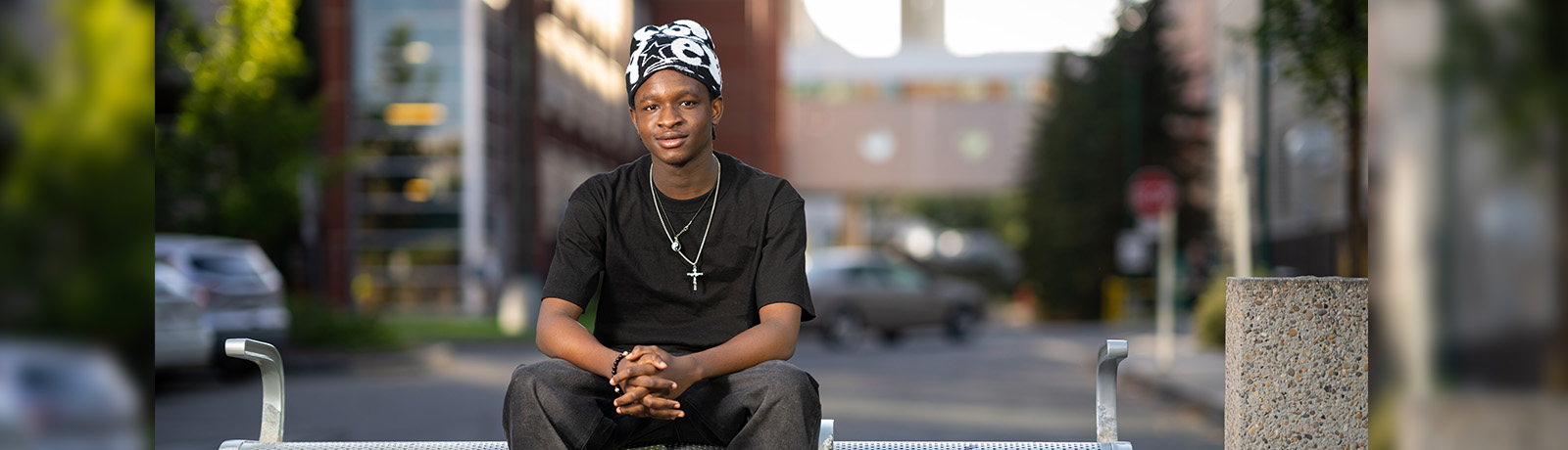 A young man sits on a bench with his fingers interlaced