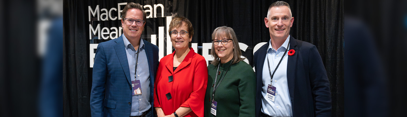 Four people stand together in front of a black background.