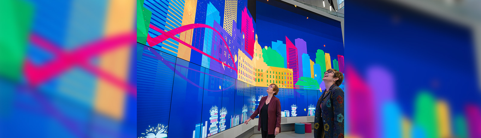 Two women look up at a massive mural of Edmonton.