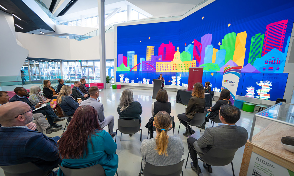 Dr. Trimbee stands at a podium in front of a crowd of people in the Edmonton Public Library.