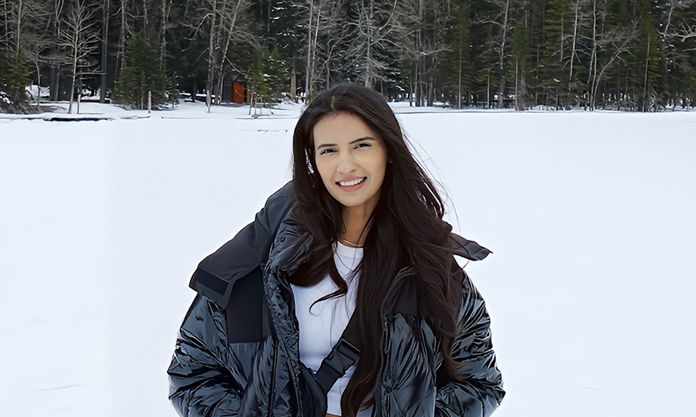 A woman stands outdoors in the winter in front of pine trees.