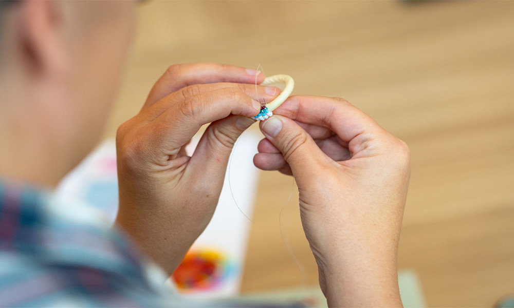 A close-up shot of hands using a needle and thread to bead around a circle.