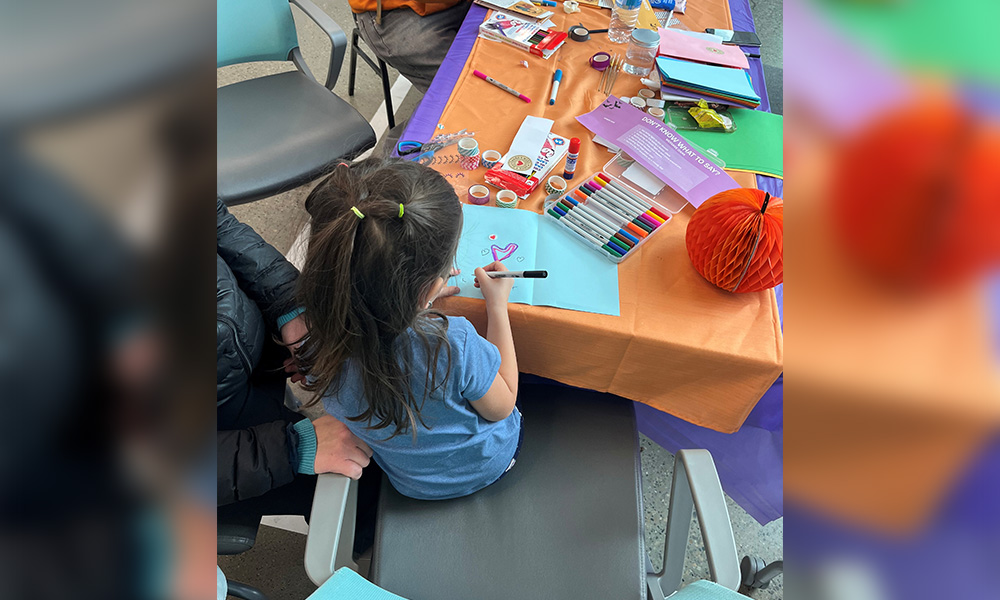 A child sits at a table and colours hearts on a piece of paper to make a card.