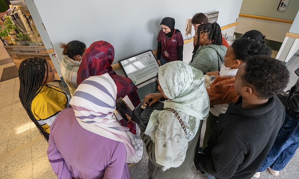 A group of people stand around a page of a story mounted to a wall.