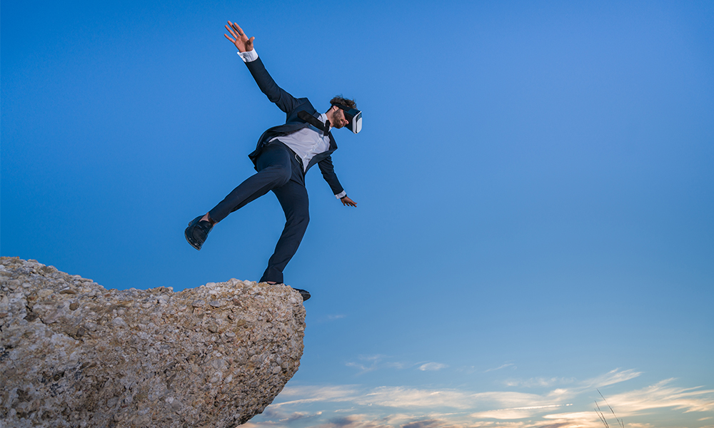 A person standing with one foot on a cliff-edge, wearing a VR headset