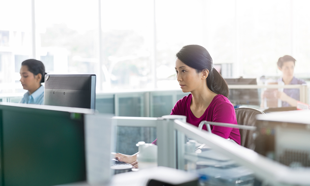 Three people sitting at cubicles, looking at screens 