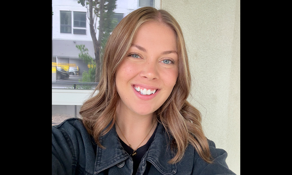 A woman smiles in front of a window in a tan stucco wall.