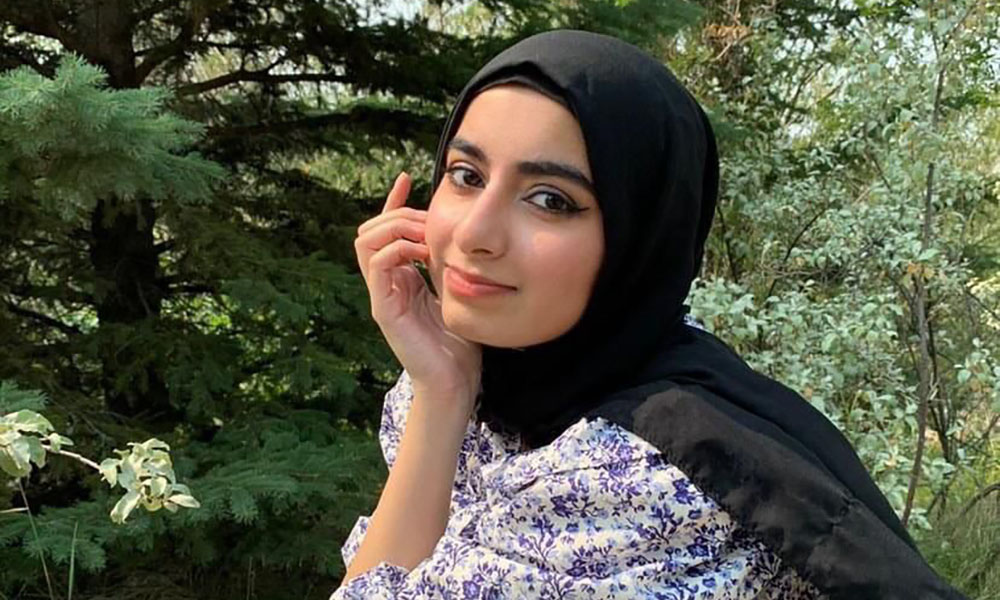 A woman sits in front of a tree, her hand touching her face