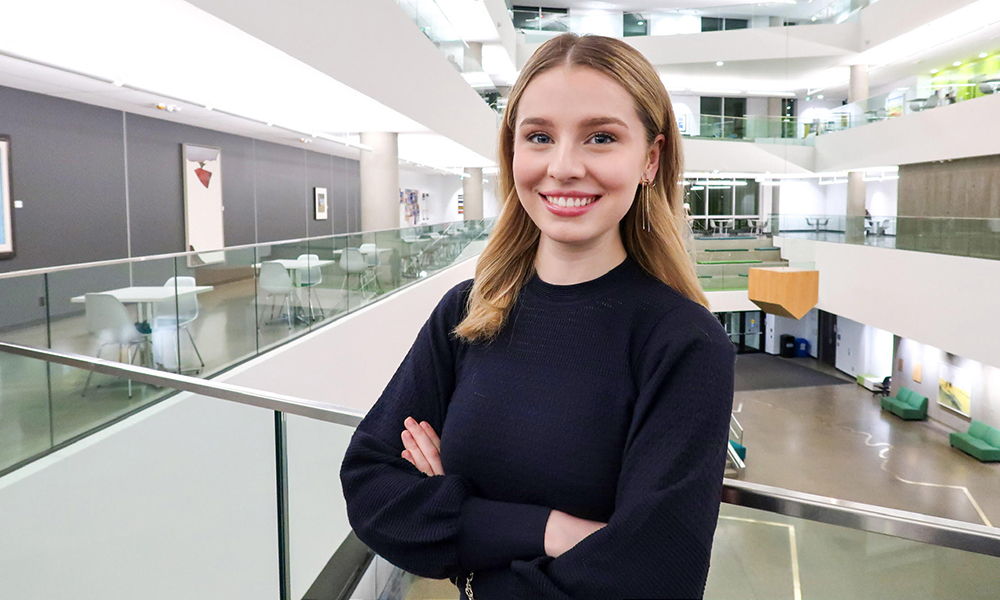 A woman stands at a glass railing, overlooking the atrium of a large building