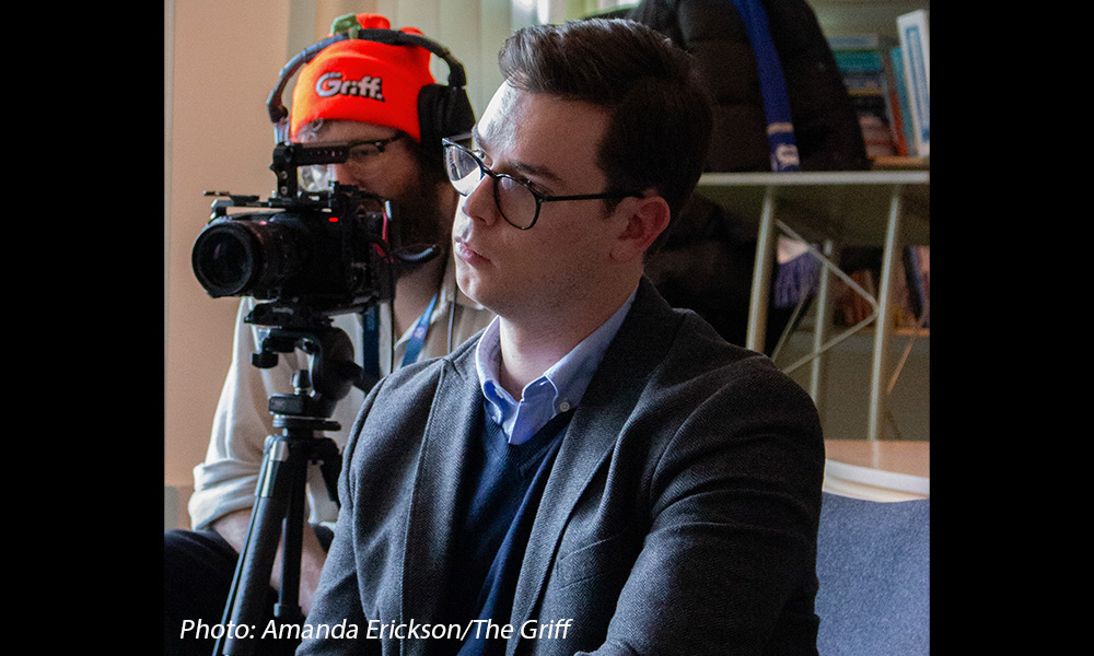 A man sits near another man who is taking video