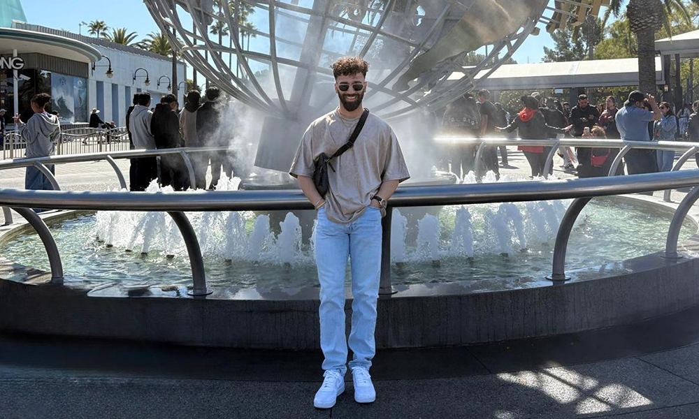 A man stands in front of a metal sculpture of the Universal Studios logo.