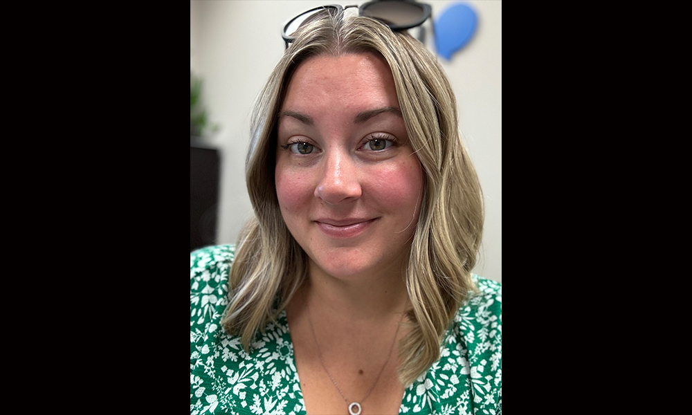 A close up of a woman wearing a green dress with white flowers, and sunglasses on her head. 