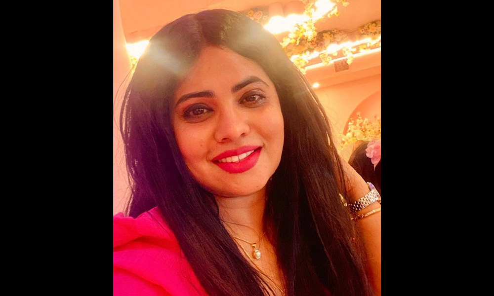 A woman wearing red smiles, a bright light behind her.