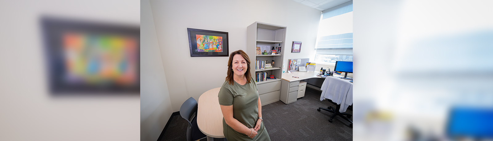 a woman leans against a table in a small, bright office,