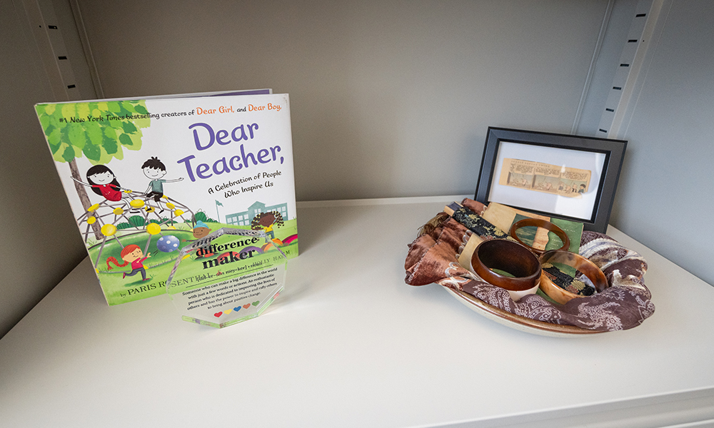 a bookshelf with a book, an award, a bowl with mementos and a framed comic strip