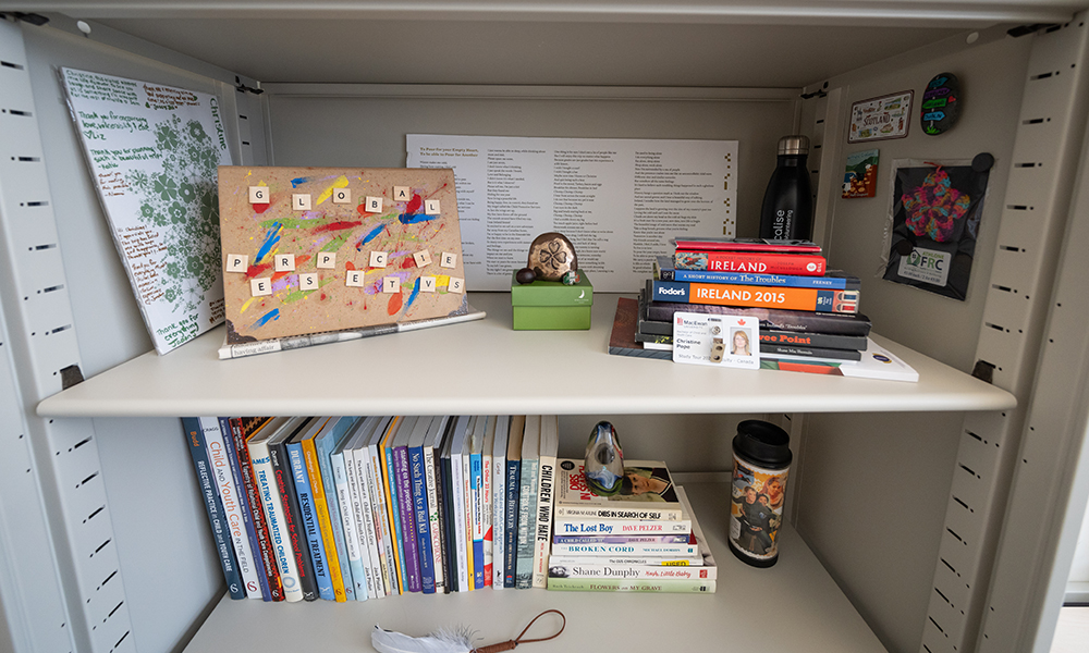 a bookshelf with various books, objects, pictures and a long poem printed on hard cardboard at the far back