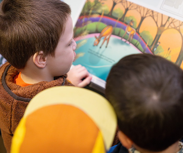 Children look at a storybook page mounted to a wall.